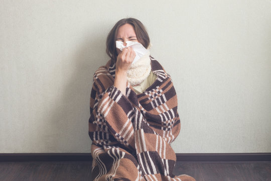 Girl blow one's nose with paper tissue. Woman in warm woolen plaid sit on floor