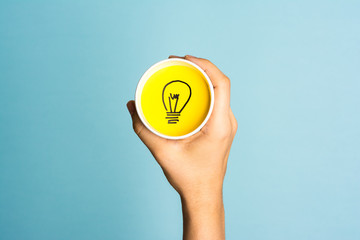 New idea concept. Hand holding a paper cup with lightbulb symbol.
