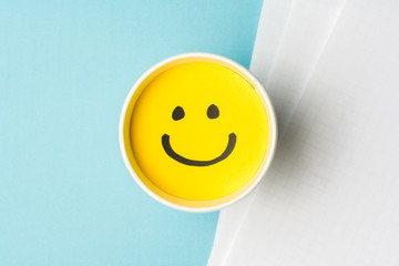 Yellow smiley face or happy emotion, on paper cup and papers over blue background.