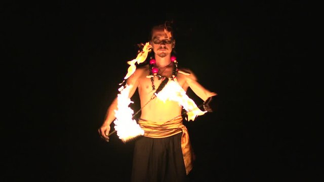 Fire show performance. Male fire performer spinning burning fire rope dart poi on long rope In front of his abs. Slow motion