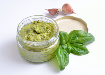 Pesto sauce in a glass jar with basil and garlic.