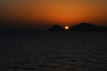 Naklejka na ściany i meble Beautiful orange sun between two mountais at the sunset time near the sea. 