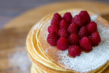 Tasty homemade pancakes with cream and raspberry. On wooden table. Village kitchen