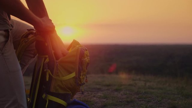 Collect things on the journey. The man puts things in a hike, puts them in a backpack. At sunset