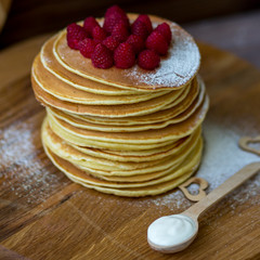 Tasty homemade pancakes with cream and raspberry. On wooden table. Village kitchen