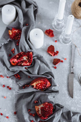 chunks of ripe red pomegranate, fork and knife on a grey kitchen towel on a grey white background with candles, seeds top view food photos