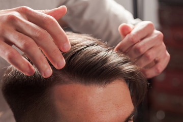 The hands of barber making haircut to young man in barbershop