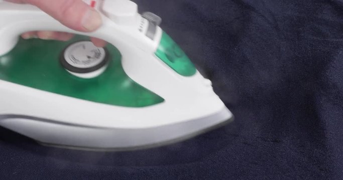 Video of ironing a wrinkled blue shirt with steam rising..