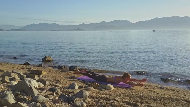 Drone Flies Past Girl Lying in Yoga Pose against Shining Sea