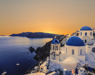 The Greek Orthodox Church on the background waters of the Aegean sea in Oia at sunset. The Island Of Santorini, Greece