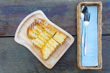 top view and close up.. Toast topped with Condensed milk on a wooden plate with cutlery in a box on wooden table