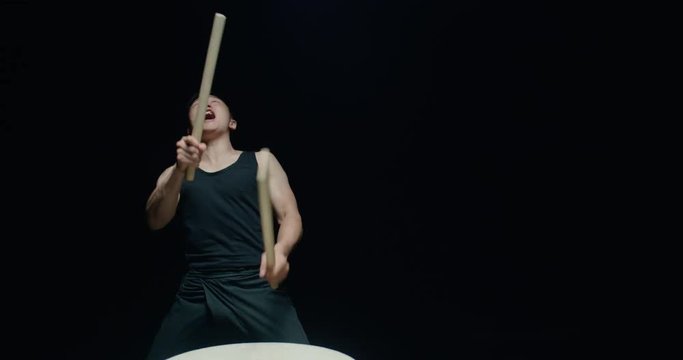performance of Taiko , Asian male drummer in black clothes is very expressive beats the rhythm on a Japanese drum,black background