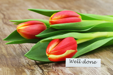 Well done card with red and yellow tulips on wooden surface
