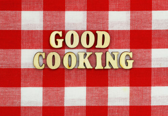 Good cooking written with wooden letters on red and white checkered cloth
