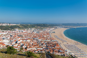 Fototapeta premium Nazare beach in Portugal in summer, people in holidays and tiles roofs of the village 