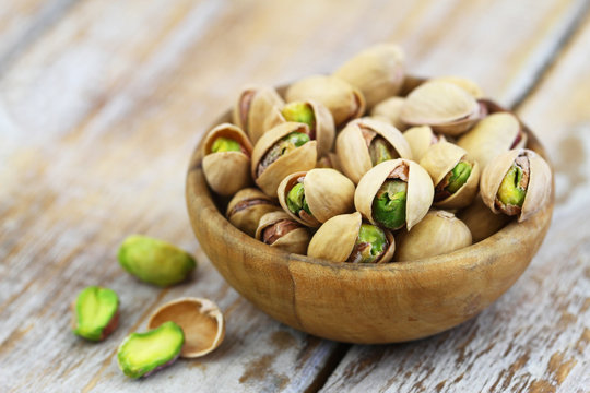 Pistachios with and without shell in bamboo bowl on rustic wooden surface
