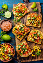 Mexican Latin American style open sandwiches. Vegetarian toasts with maize, avocado, tomatoes on wooden board. Rustic wooden blue background. Top view