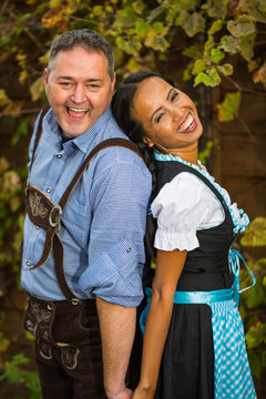 Oktoberfest - couple in traditional bavarian clothes is standing in front of a grapevine 