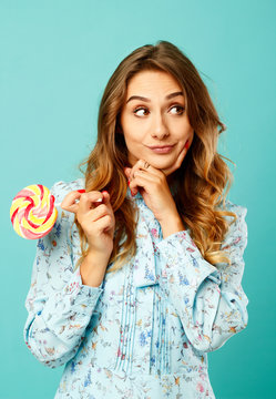 Young pretty smiley woman holding lollipop in hands over blue background