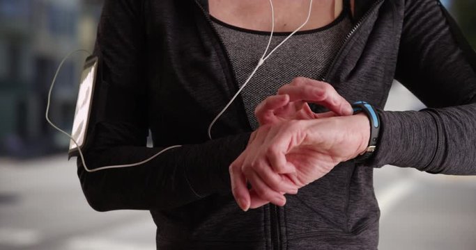 Close up of woman lifting arm up to use smart watch after jog outside. Female jogger wearing modern tracking device. 4k 