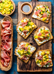 Fototapeta na wymiar Toasts with cream cheese, ham jamon serrano and mango served on wooden board with red wine, blue wooden rustic background, top view