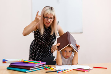 the teacher screams at the little schoolgirl. little girl with a closed book sitting at a desk in...