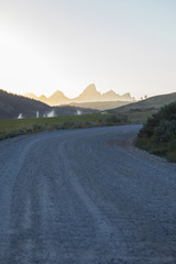 dirt road through some valley farms leading to giant mountains