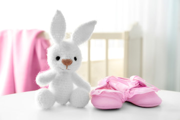 Knitted toy bunny and baby shoes on table