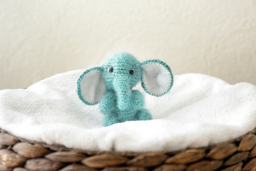 Cute knitted toy elephant in wicker basket on light background