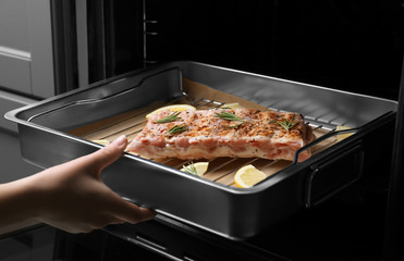 Young woman putting baking tray with pork ribs into oven