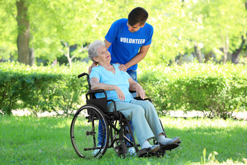 Fototapeta premium Happy senior woman on wheelchair with young male volunteer outdoors