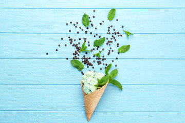 Composition of delicious mint chocolate chip ice cream in waffle cone and fresh leaves on wooden background