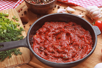 Frying pan with tasty spicy sauce on wooden board