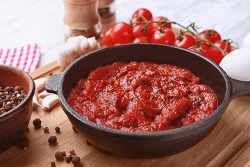 Frying pan with tasty spicy sauce on wooden board