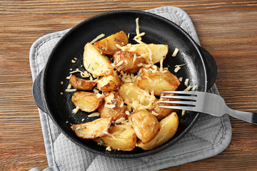 Delicious potato with cheese in frying pan on pot holder on table