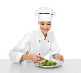 Young female chef making salad on white background
