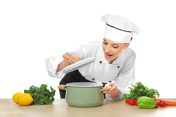 Young female chef near table with saucepan and different products, on white background