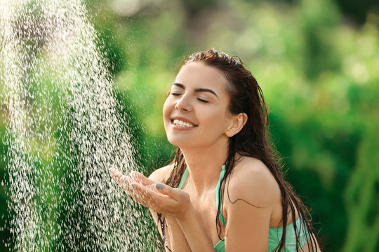 Beautiful young woman taking shower outdoors