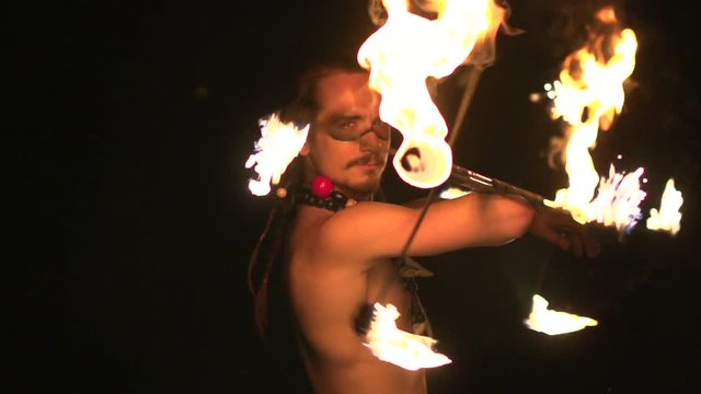 Fire show performance. Handsome male fire juggler performing contact manipulation with fire baton with several wicks. dragon staff. Slow motion