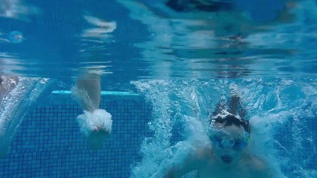 Children jumping into deep swimming pool in slow motion with underwater camera. Girl breathes out air bubbles