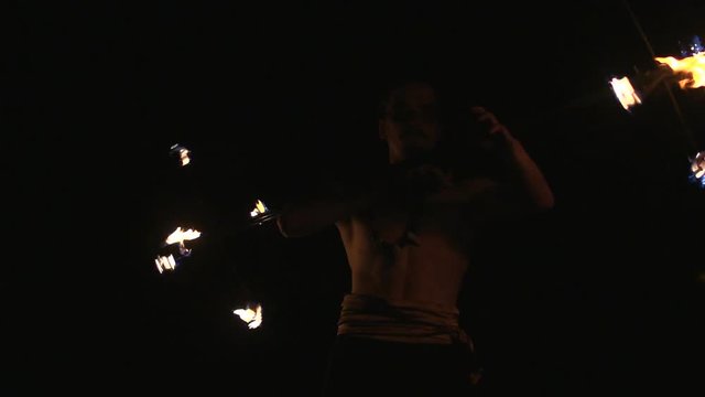 Fire show performance. Handsome male fire juggler performing with fire baton with several wicks, dragon staff. Slow motion