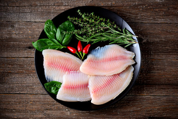 Fresh raw fillet of tilapia fish with thyme, rosemary, basil and chili pepper.
