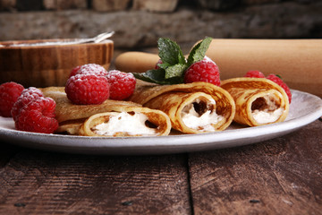 Homemade crepes served with fresh raspberrries and powdered sugar on rustic wooden table