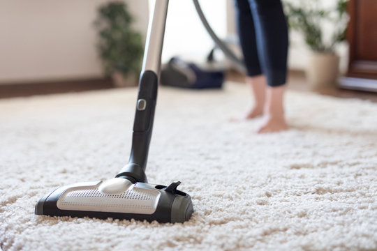 Woman using a vacuum cleaner while cleaning carpet in the house.