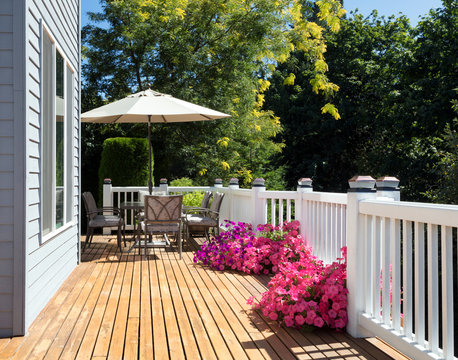 Home cedar deck during bright summer day with blooming garden of flowers