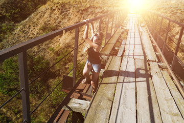 Beautiful young girl falls through the old rustic bridge. Grip for the handrail. Anxious and frightened face. Fear for life. Fantastic light