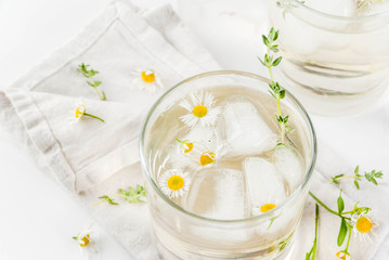Summer refreshing drinks, infused herbal water, iced tea. Chamomile Honey and Whiskey Cocktail with thyme in glasses, on a white marble table. Copy space