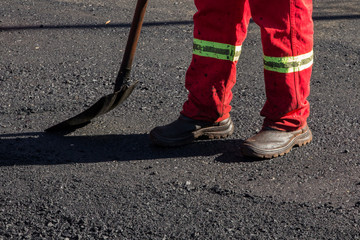 Homem trabalhando no asfalto com botas e pá 