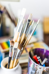 Macro closeup of many clean paintbrushes in cup on artist desk