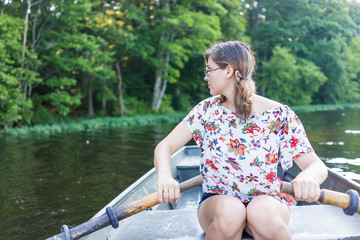 Young woman with glasses rowing boat on lake in Virginia during summer looking to side